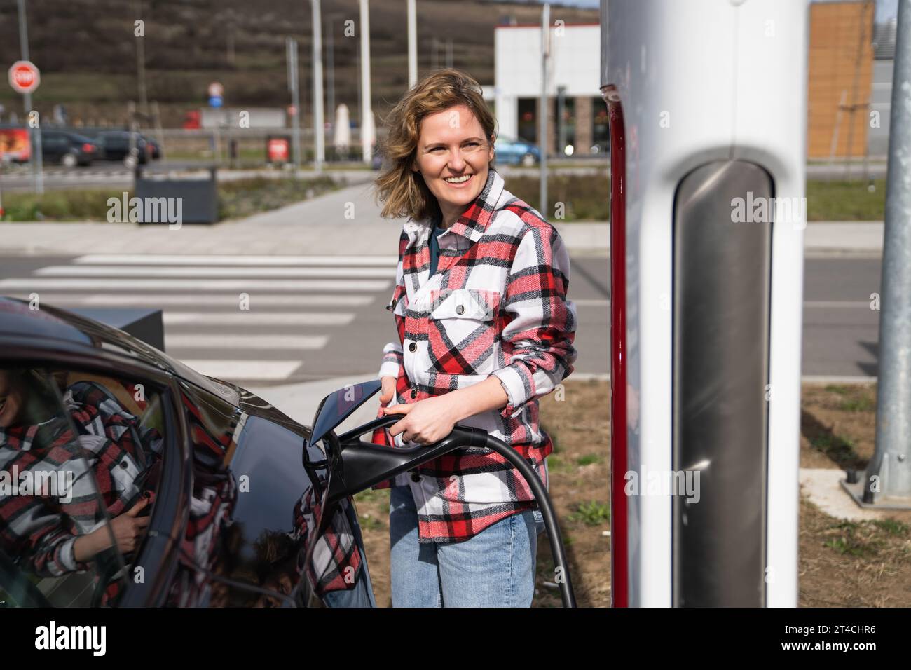 Woman in a plaid shirt charging an electric car. Stock Photo