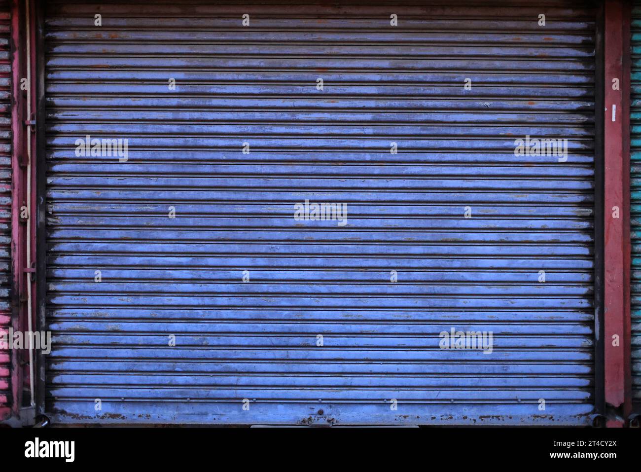 A close-up of a vibrantly colored, yet aged and rust-streaked metal shutter, capturing the essence of urban wear and tear. Stock Photo