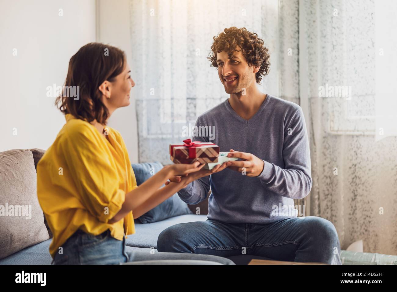 Portrait of young happy couple. Woman is giving gift to her man. Stock Photo