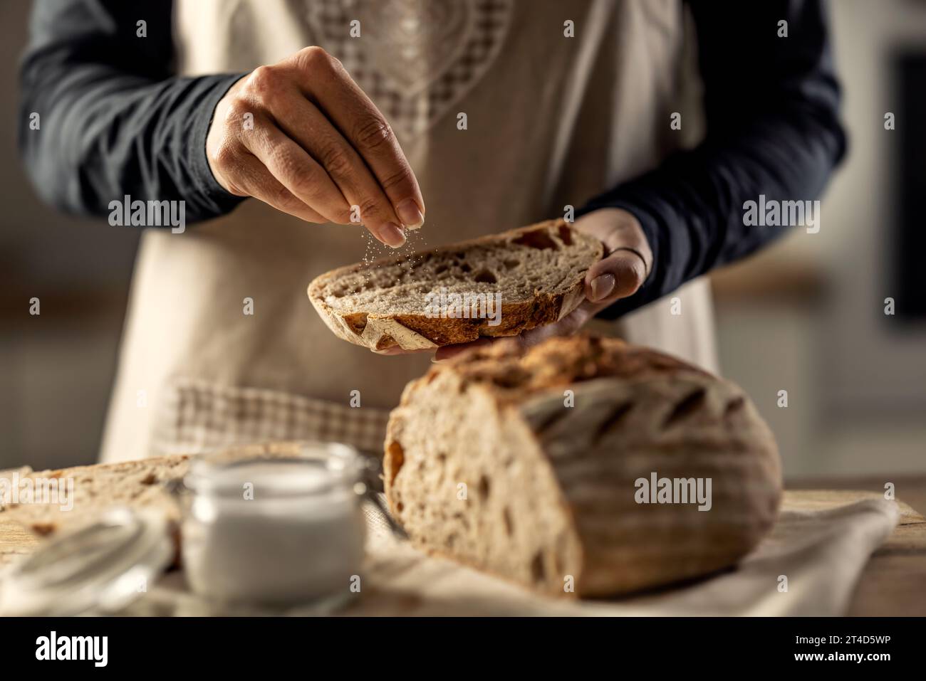 Female cook salting a fresh slice of bread - Close Up. Stock Photo