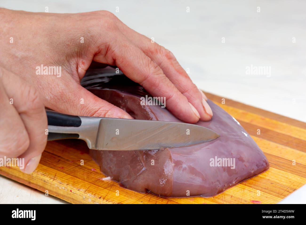 Woman hand cutting beef liver on cutting board using knife Stock Photo