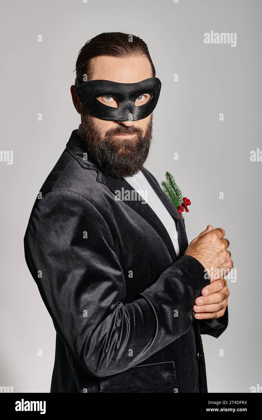 Christmas Masquerade ball, handsome bearded man in carnival mask and elegant suit on grey backdrop Stock Photo