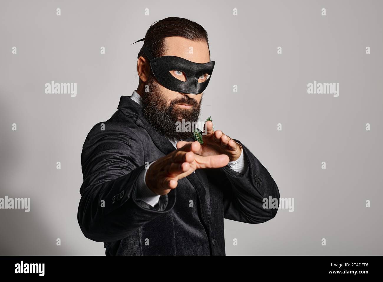 Christmas Masquerade ball, handsome bearded man in carnival mask and elegant suit on grey backdrop Stock Photo