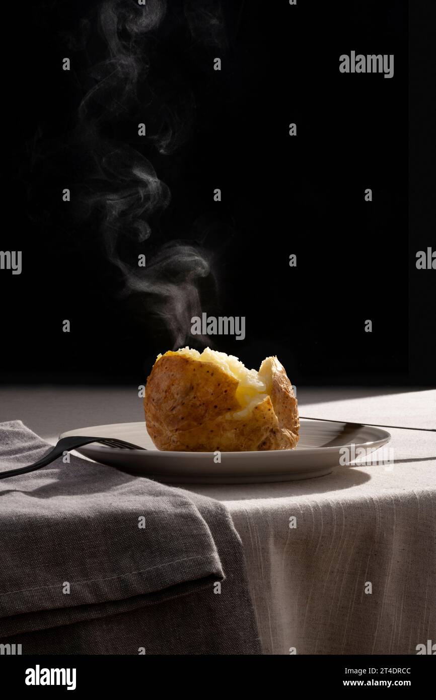 Steaming roasted potato on a plate with contrast backlight and monochromatic background Stock Photo