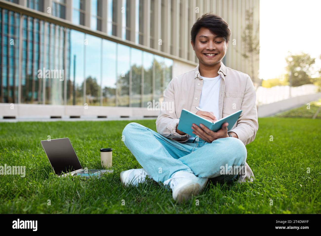 Happy young asian guy student with laptop sitting outdoors Stock Photo