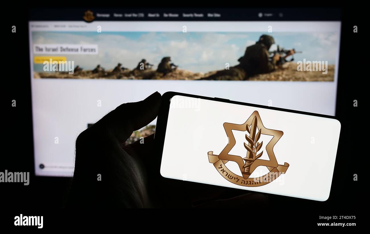Person holding mobile phone with logo of national military Israel Defense Forces (IDF) in front of web page. Focus on phone display. Stock Photo
