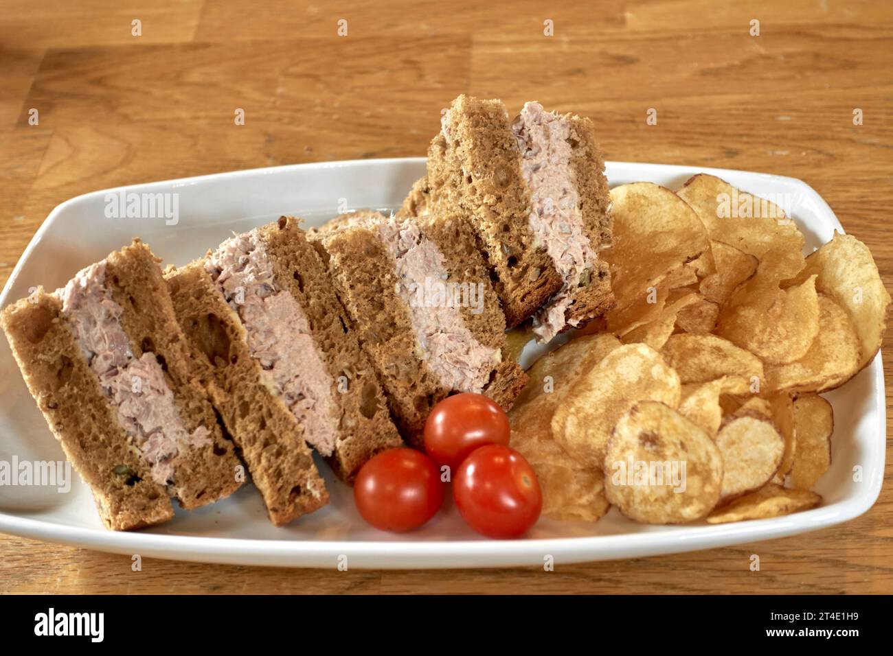 Tuna sandwich, brown bread, potato crisps, cherry tomatoes Stock Photo