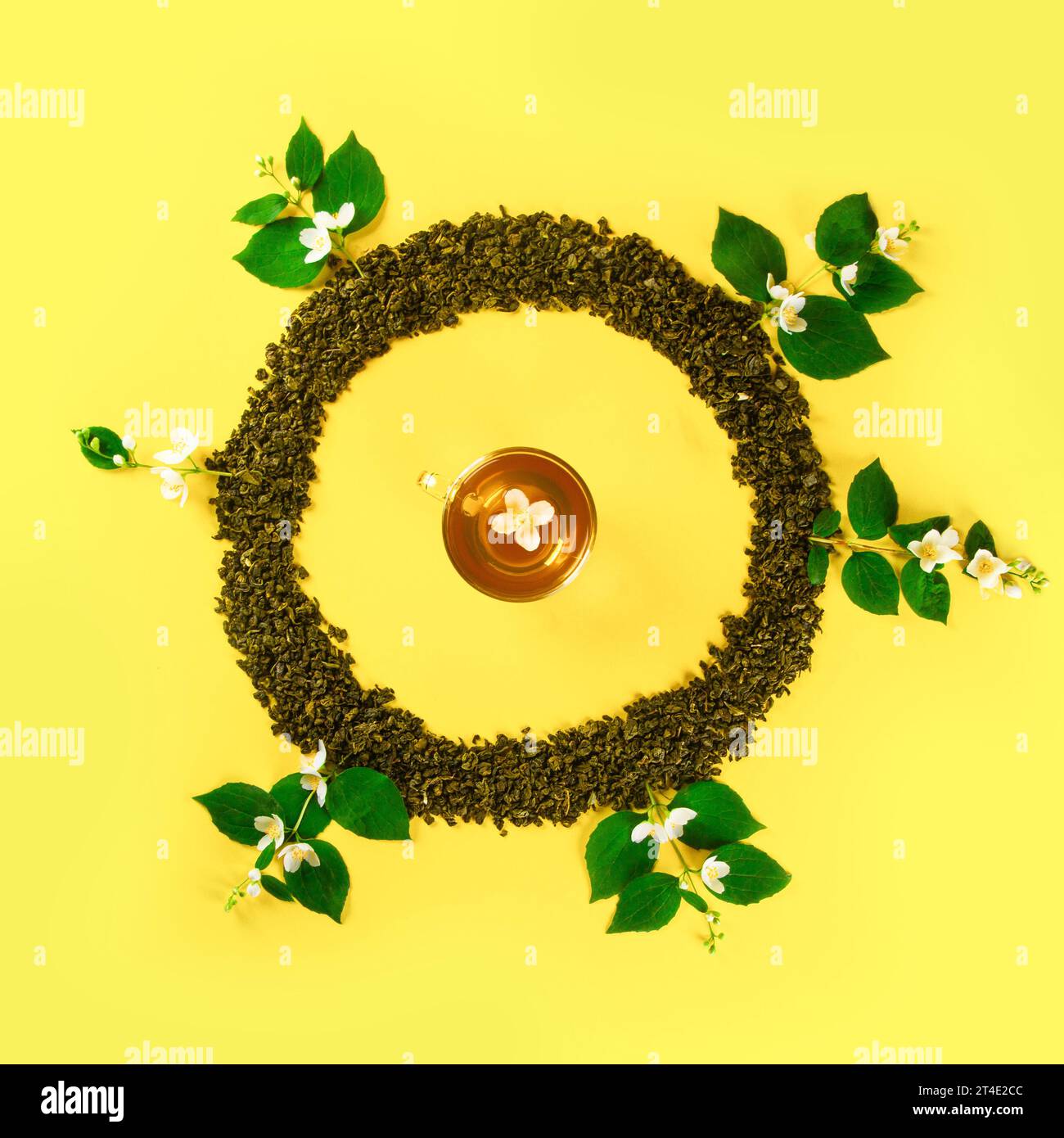 Mockup of dried tea leaves and fresh jasmine flowers shaped in round Frame with tea cup in center isolated on plain yellow background Stock Photo