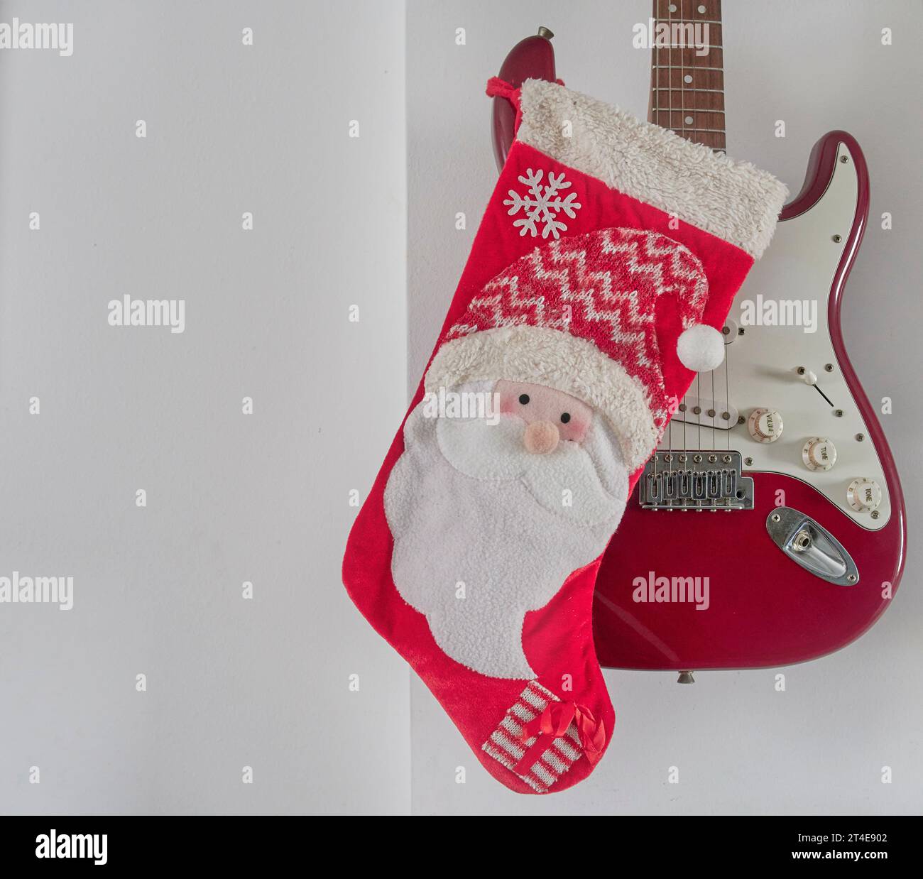 Christmas decoration, red santa sock hanging from a red electric guitar on a white wall. Christmas concept. Copy space. Horizontal Stock Photo