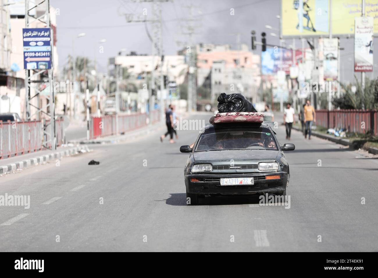 Palestinians drive a car loaded with belongings while smoke billows in the background as they