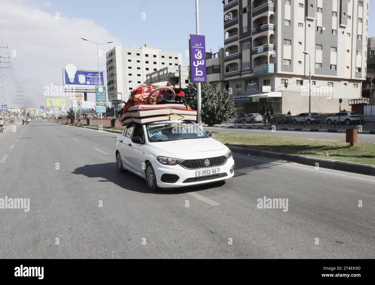 Palestinians drive a car loaded with belongings while smoke billows in the background as they