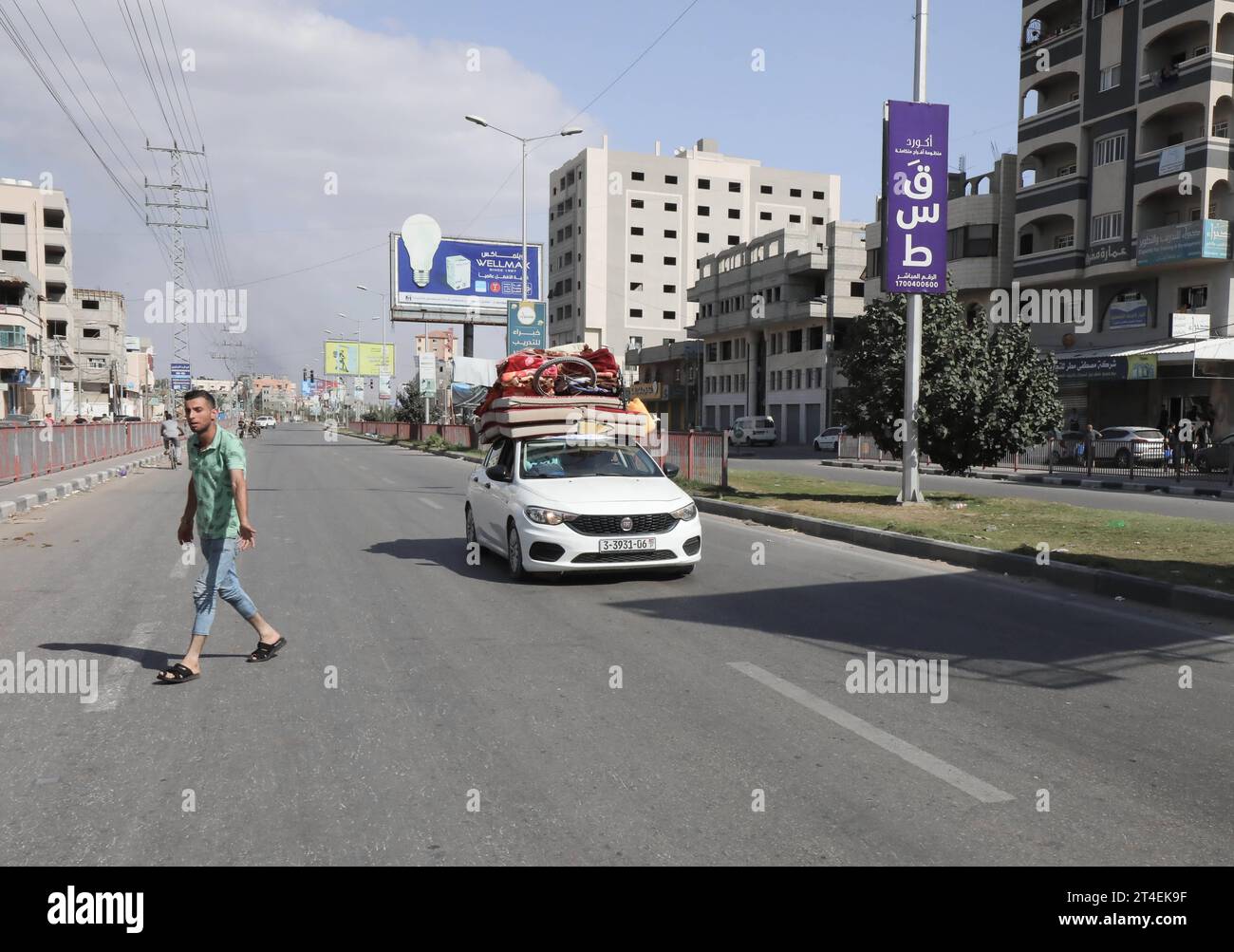 Palestinians drive a car loaded with belongings while smoke billows in the background as they