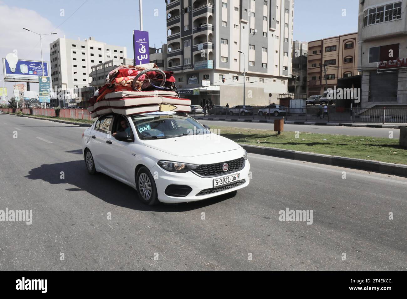 Palestinians drive a car loaded with belongings while smoke billows in the background as they