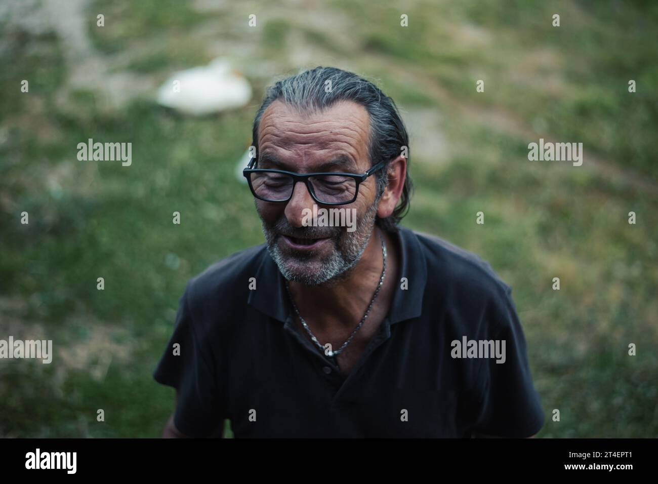 A Serbian senior, 60 and vibrant, in glasses and long hair, enjoying the outdoors with animated conversations and a contagious smile Stock Photo