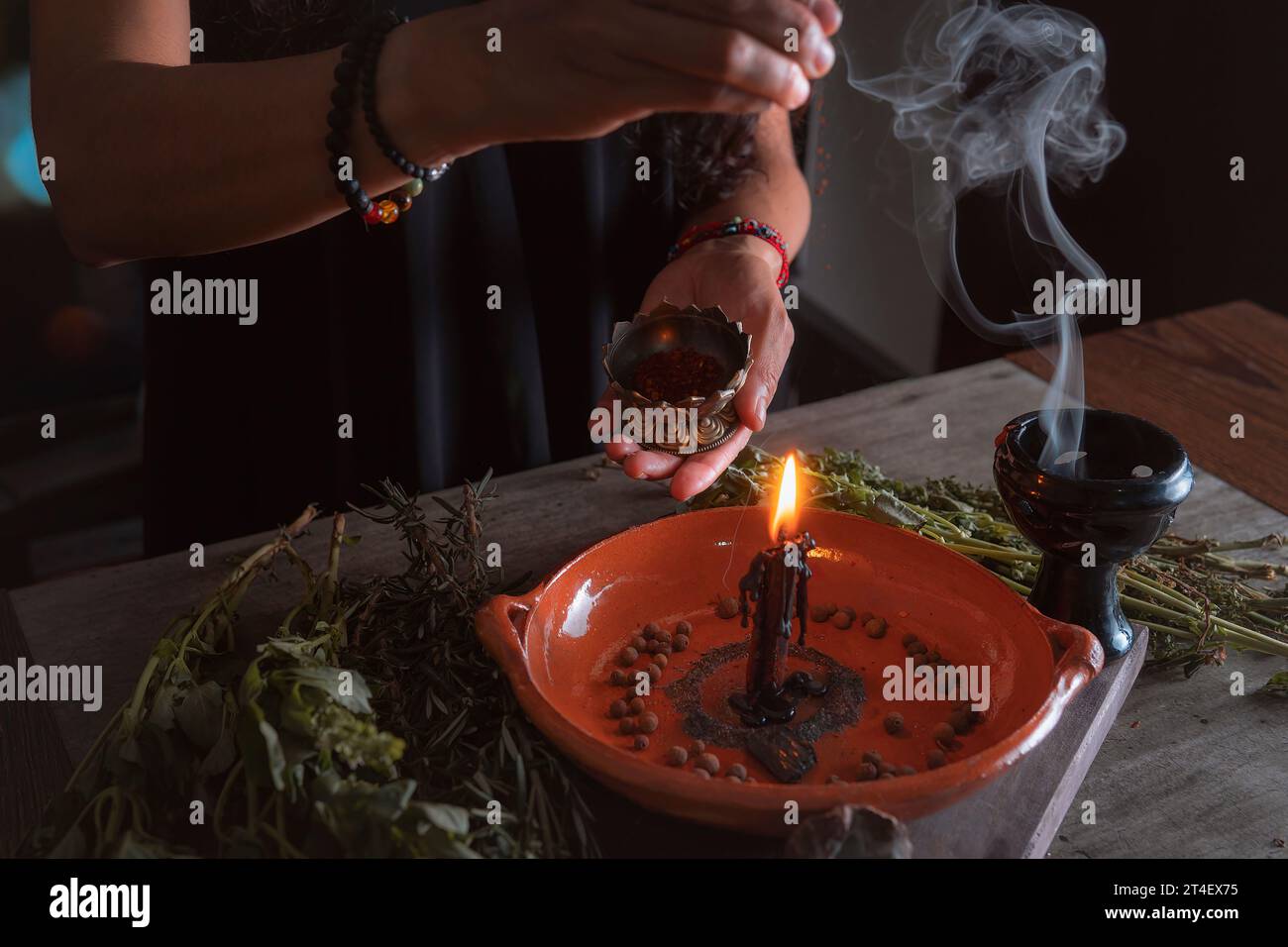 woman doing traditional ritual with black candle sea salt pepper in clay plate with herbs and incense and energy management with fire Stock Photo