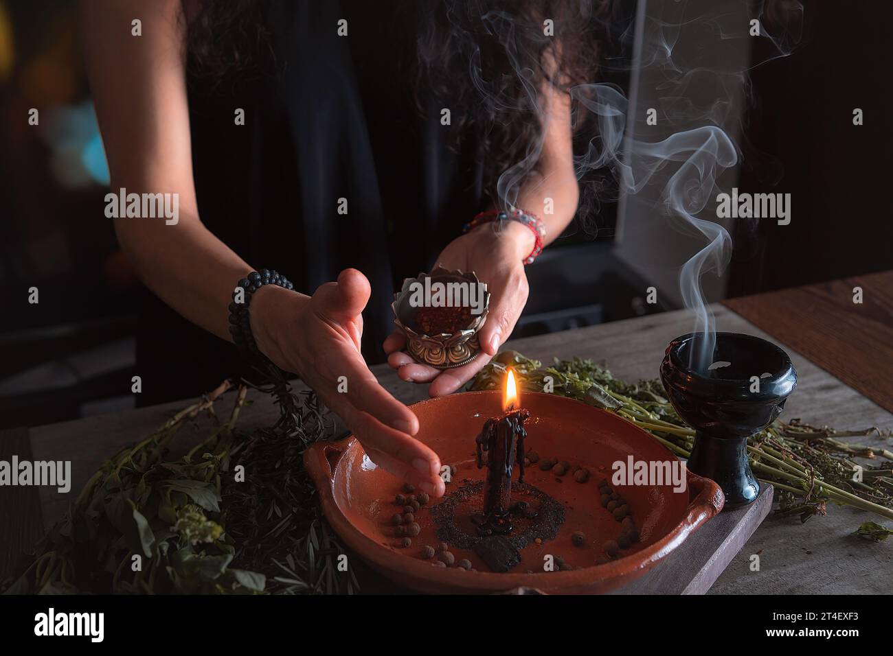 woman doing traditional ritual with black candle sea salt pepper in clay plate with herbs and incense and energy management with fire Stock Photo