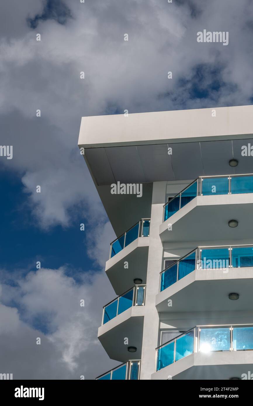 An apartment building, hotel shot from below against a blue but cloudy sky, whits with blue windows Stock Photo