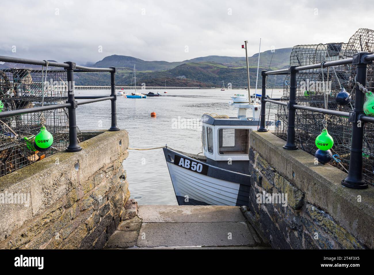 A fishing boat seen moored by the waters edge in Barmouth harbour pictured on 22 October 2023 between stacked lobster and crab pots. Stock Photo