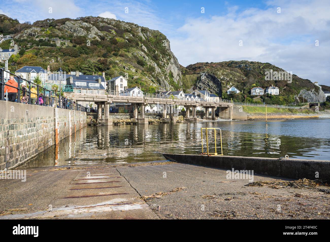 A slipway pictured on the edge of Barmouth Harbour on the Welsh coast backed by the rugged hills and mountains as tourists wonder along the top on 22 Stock Photo