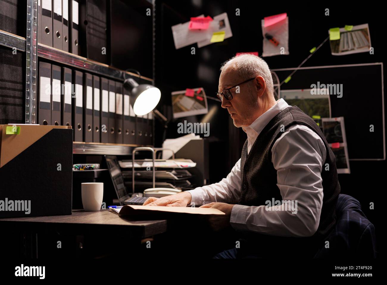 Elderly police officer analyzing confidential federal files, working at criminal investigations in arhive room. Senior private detective checking missing person case, looking at victim report Stock Photo
