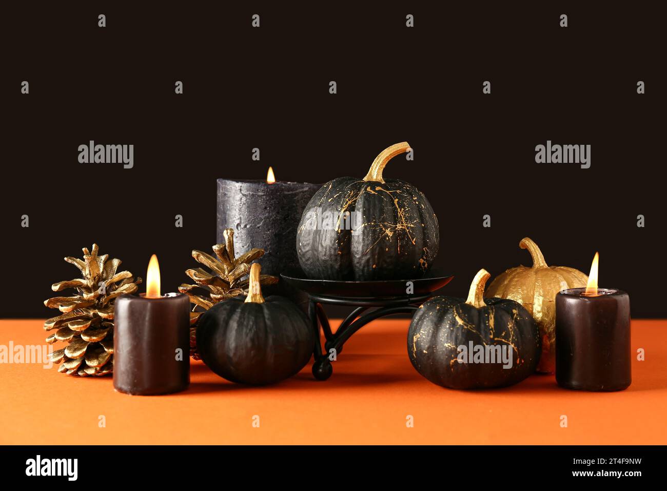 Painted pumpkins with golden cones and candles on orange table near ...