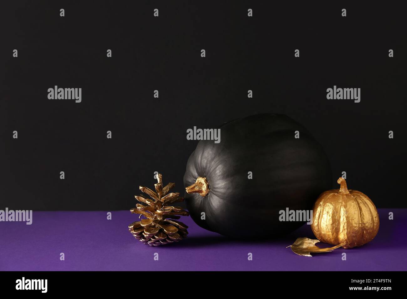 Painted pumpkins with golden cone and leaf on purple table near black ...