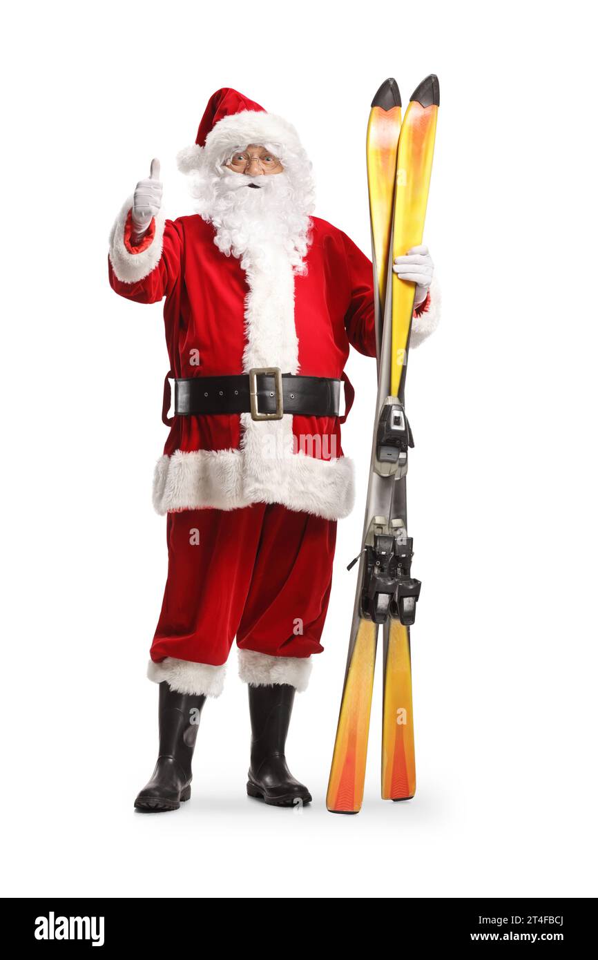 Full length portrait of Santa Claus holding a pair of skis and gesturing thumbs up isolated on white background Stock Photo