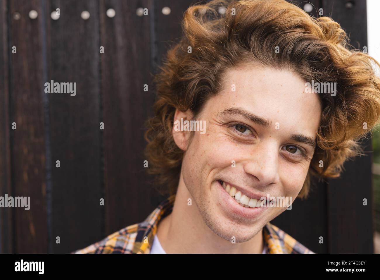 Portrait of happy caucasian man with curly hair at balcony over wooden wall Stock Photo