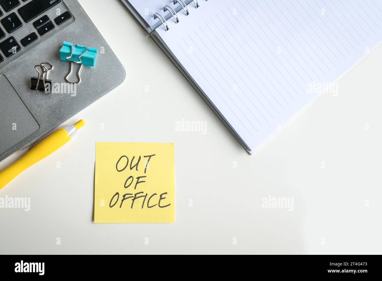 Top view of laptop and notepad with Out Of Office message written on a yellow adhesive paper. Stock Photo