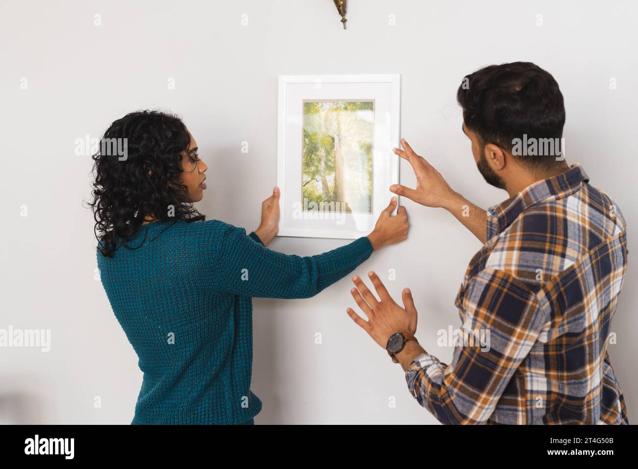 Focused biracial couple hanging picture on wall in living room at home Stock Photo