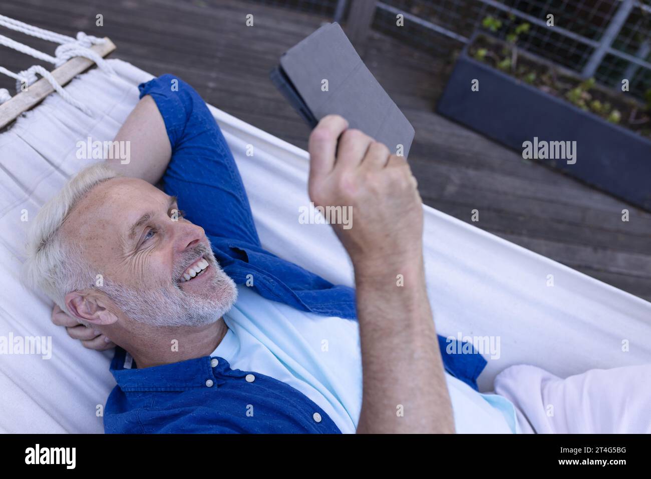 Happy senior caucasian man lying in hammock and using tablet Stock Photo