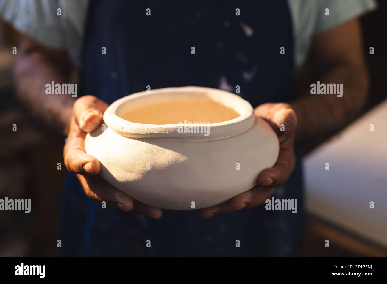 Hands of senior biracial potter holding clay vase in pottery studio Stock Photo