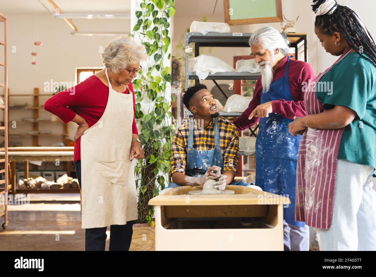 Happy african american potter using potter's wheel and discussing with others in pottery studio Stock Photo
