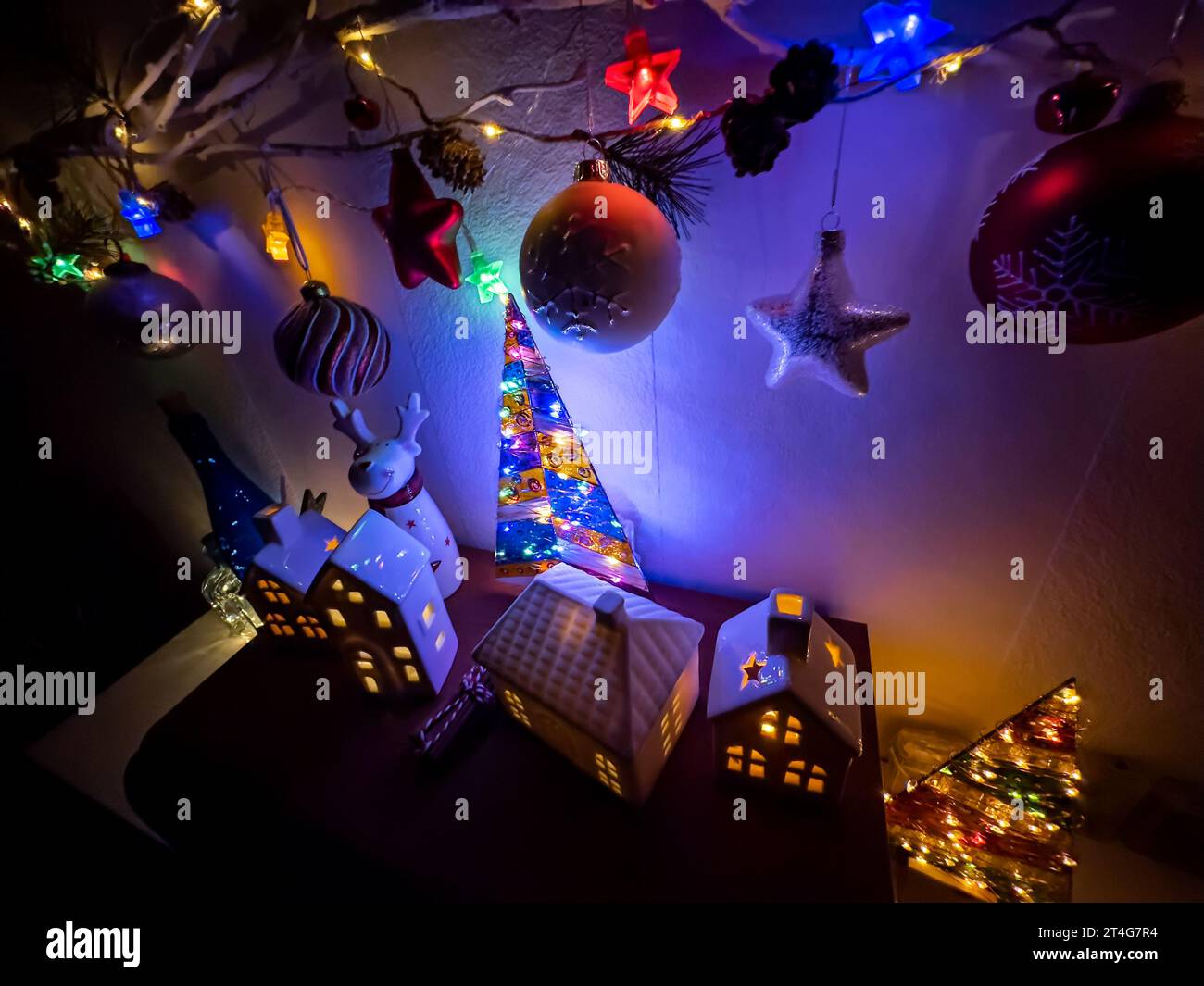 new year decorations with christmas tree balls hanging on twig and illuminated toy houses. Stock Photo