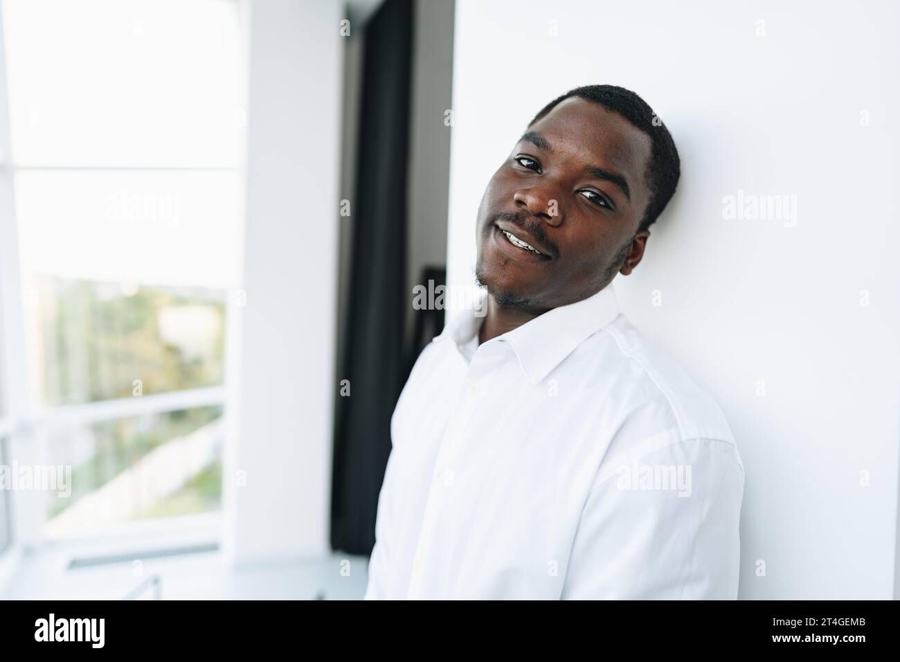Young african man in white shirt and glasses posing near large window ...