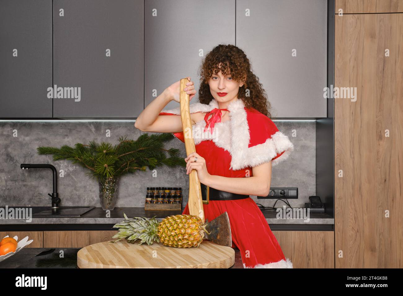 Young woman in Christmas red dress leaning on an axe in the kitchen Stock Photo