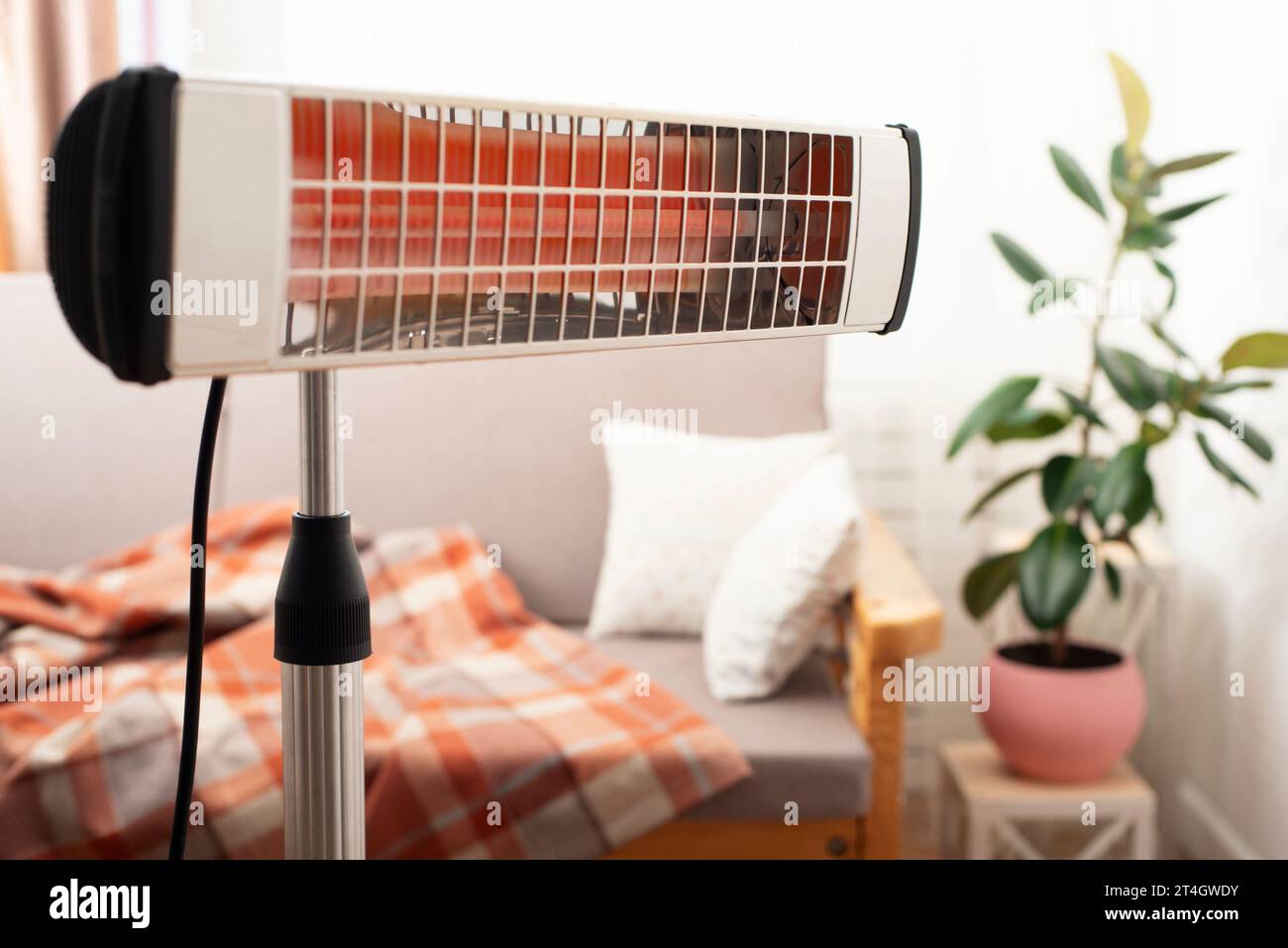 Electric infrared heater warming up living room with sofa and potted plant at background Stock Photo