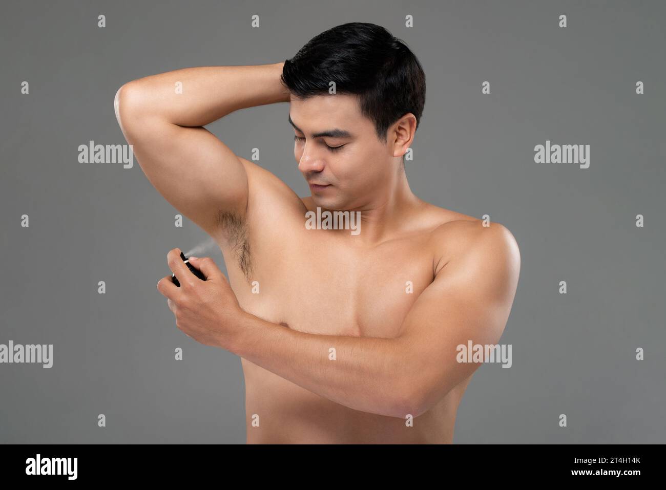 Shirtless handsome man spraying underarm with deodorant in light gray isolated studio background Stock Photo
