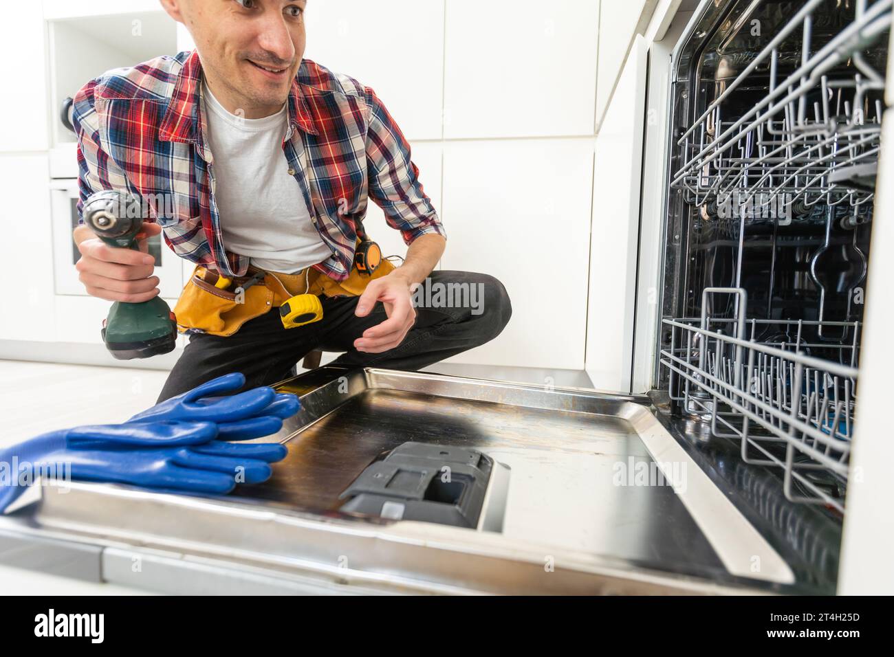 Worker using screwdriver to repair dishwasher at home stock photo Stock Photo