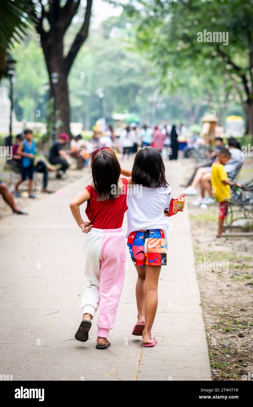 Two beautiful Filipino girls clearly best friends saunter merrily through  Rizal Park, Ermita, Manila, The Philippines. Stock Photo