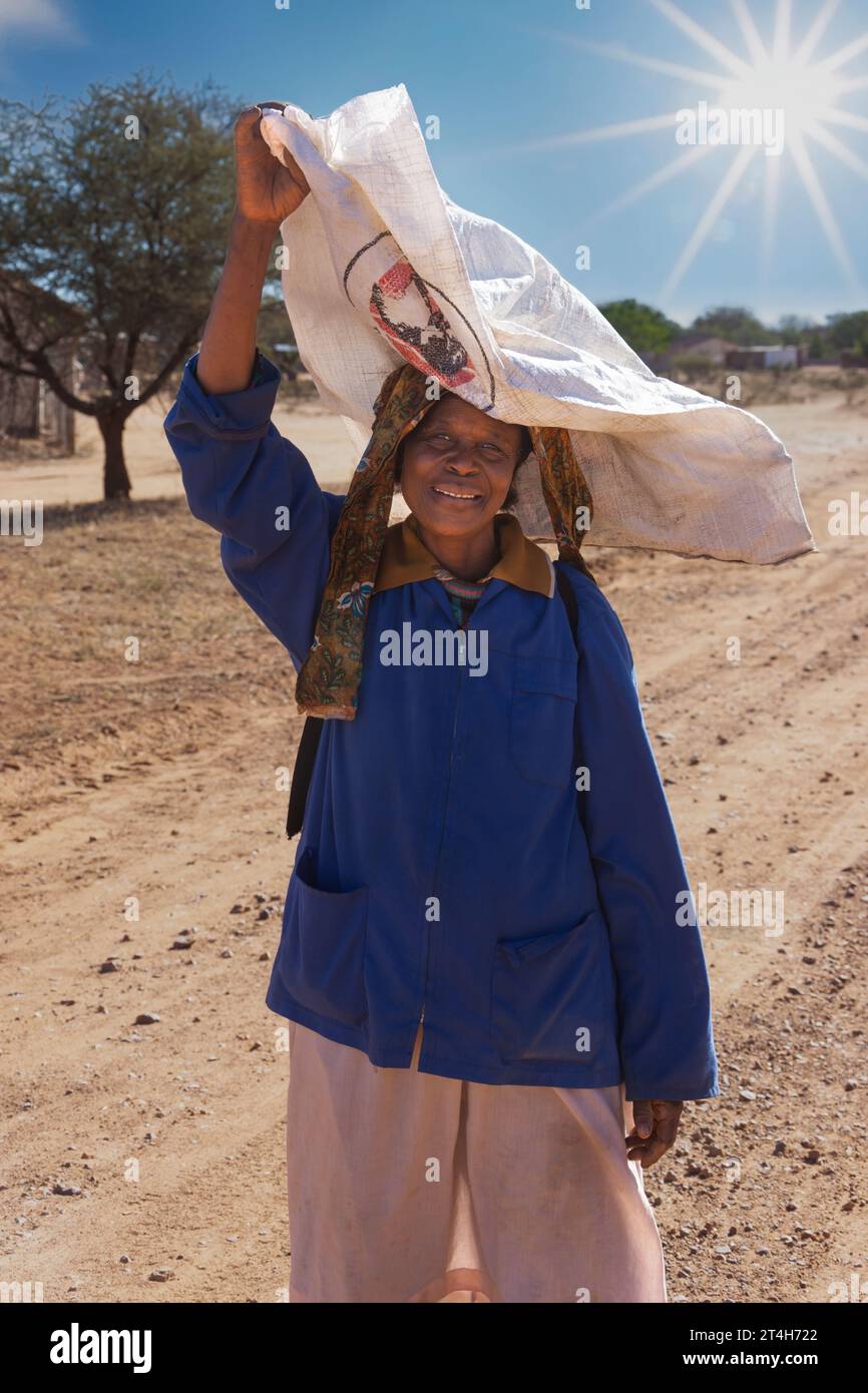 elderly african woman ,carry a sack on her head , walking on a dirt road in the village Stock Photo