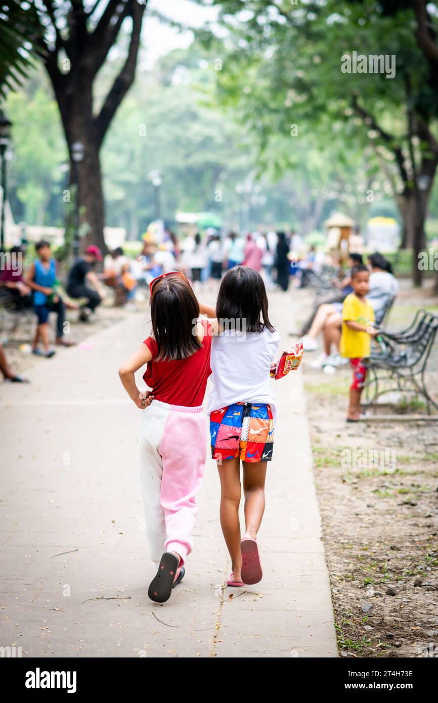 Two beautiful Filipino girls clearly best friends saunter merrily through  Rizal Park, Ermita, Manila, The Philippines. Stock Photo