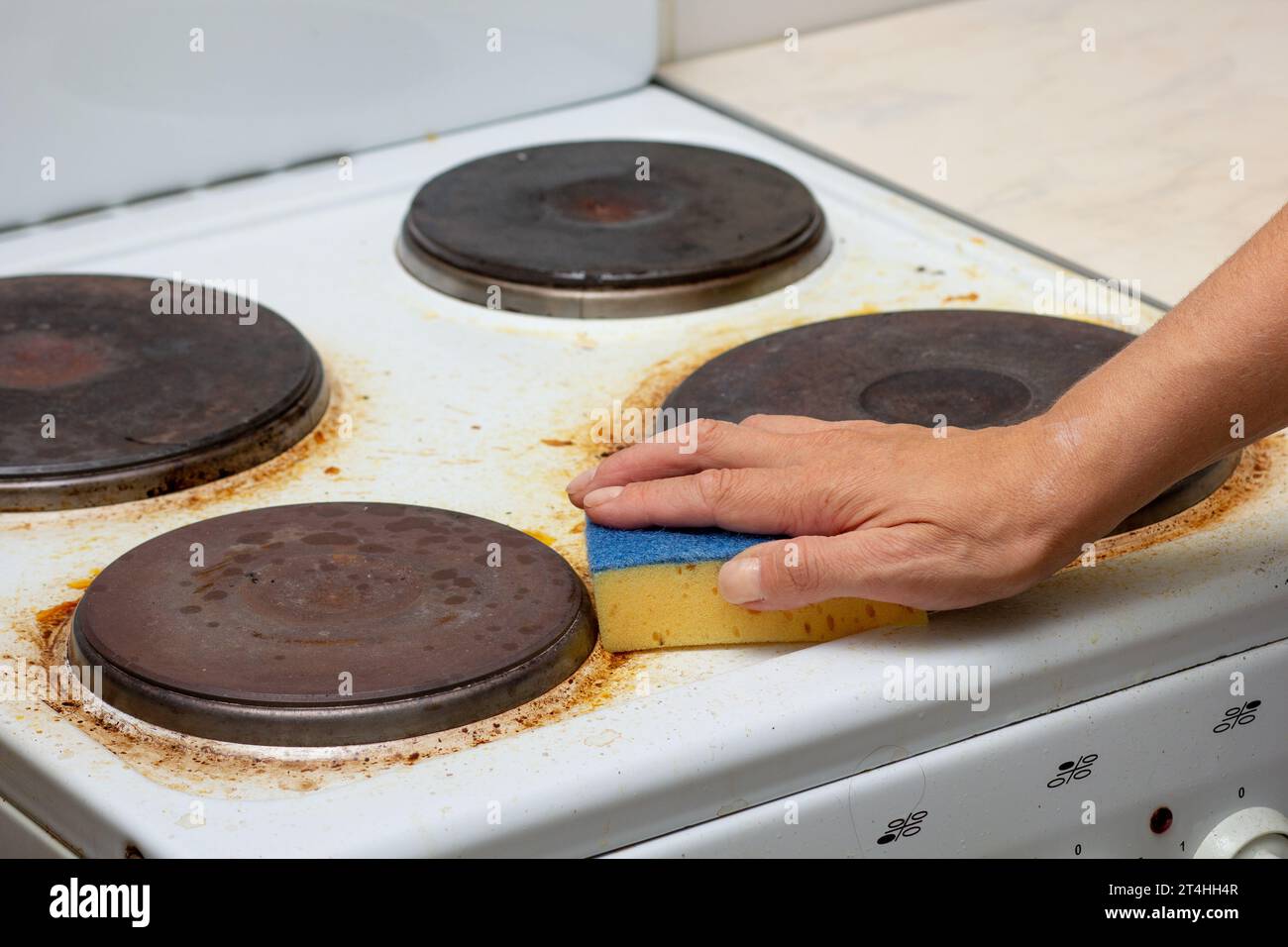 Woman hand remaining burnt stains on dirty white electric stove scrubbing using sponge Stock Photo