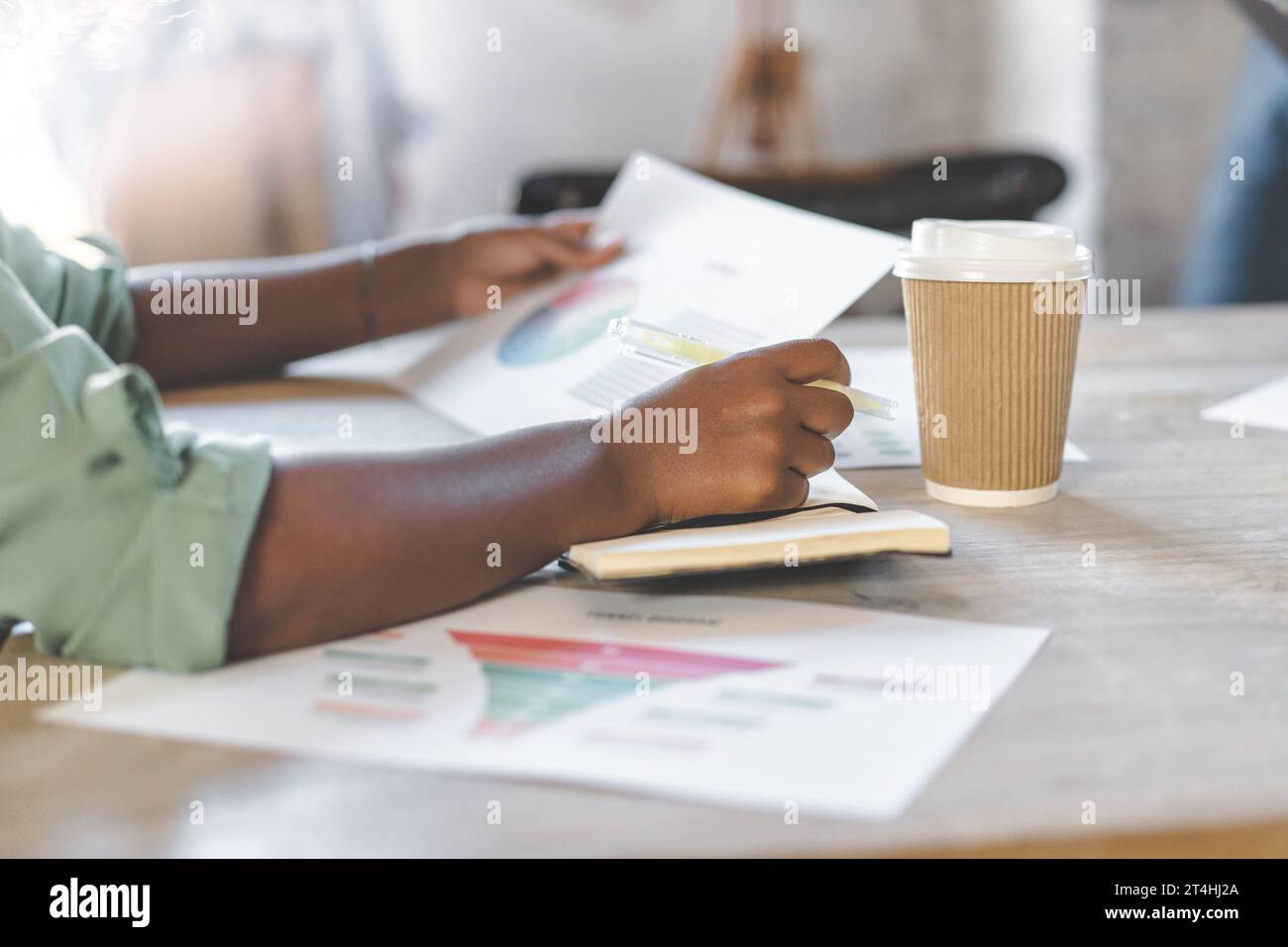 A detailed shot captures hands pointing at colorful graphs, suggesting a deep analysis or study session. Adjacent to the hands, a notebook is ready fo Stock Photo