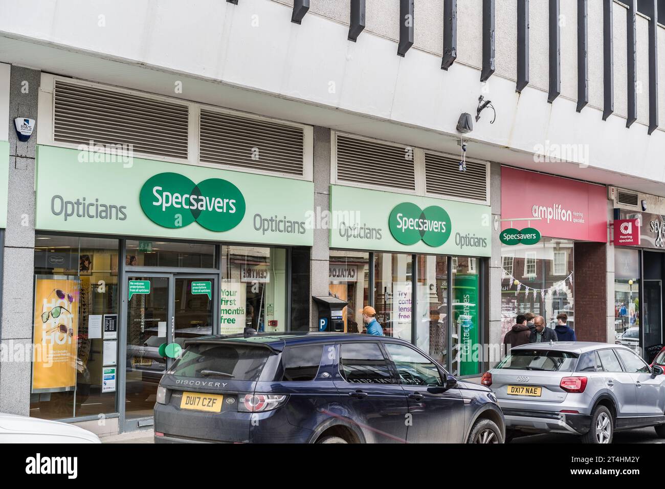Shrewsbury, Shropshire, England, May 1st 2023. People passing Specsavers opticians and Amplifon audiologists in street with parked cars. Stock Photo