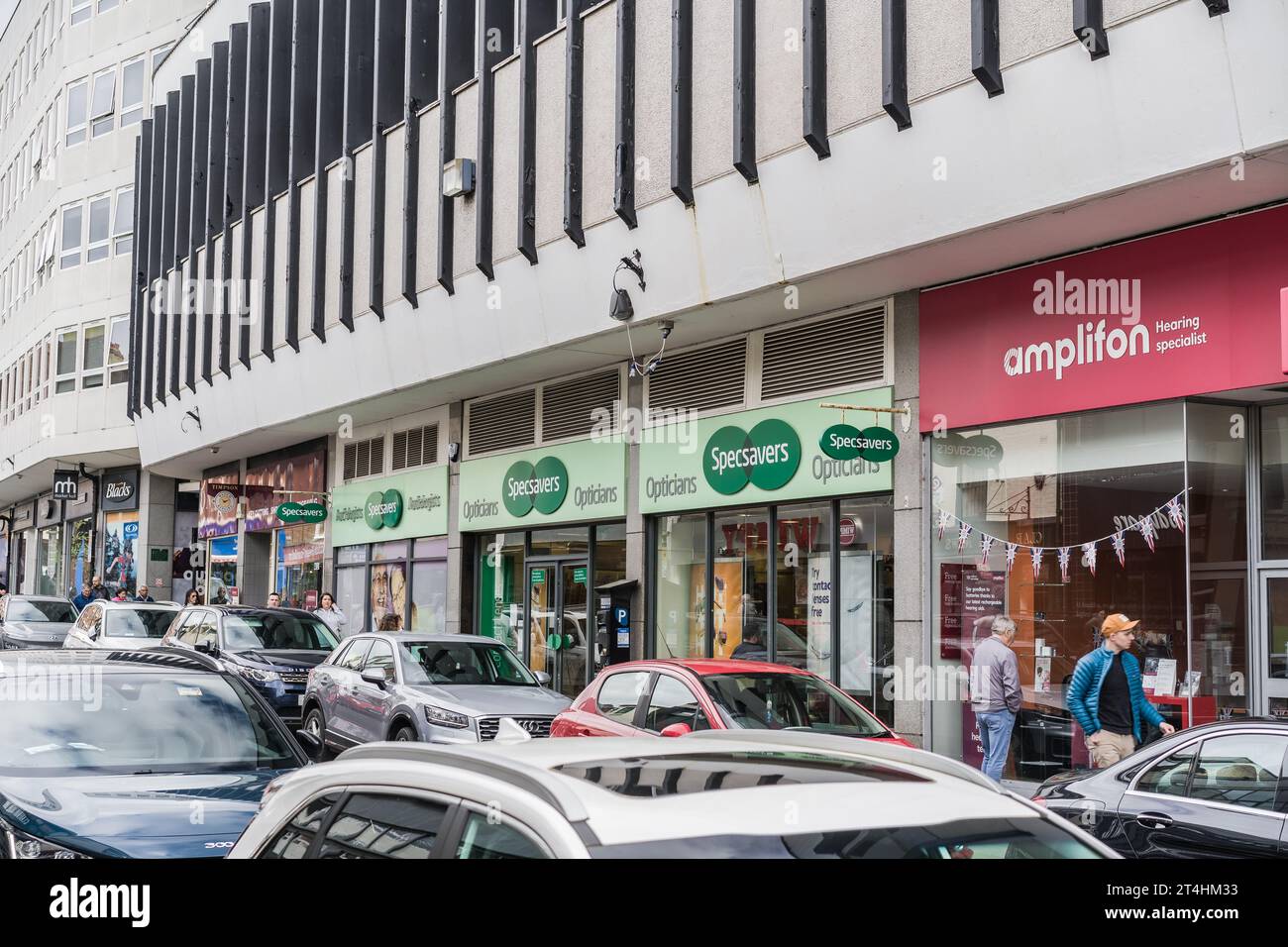 Shrewsbury, Shropshire, England, May 1st 2023. People passing Amplifon audiologists and Specsavers opticians in street with parked cars. Stock Photo