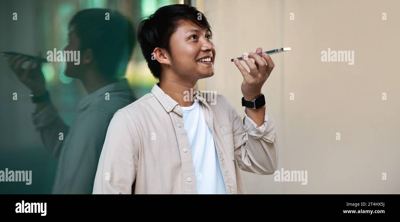 Smiling asian guy using phone voice recognition to send message Stock Photo