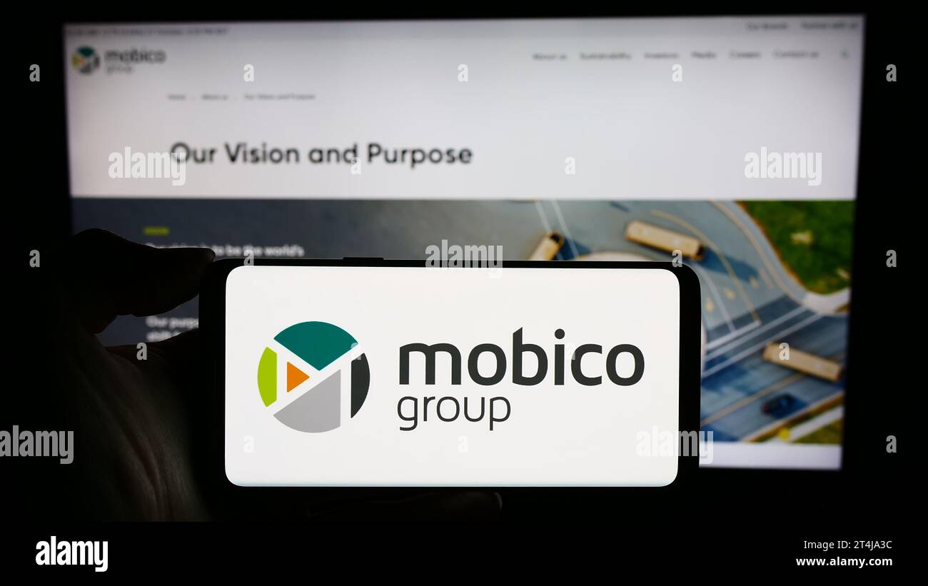 Person holding smartphone with logo of British public transport company Mobico Group in front of website. Focus on phone display. Stock Photo