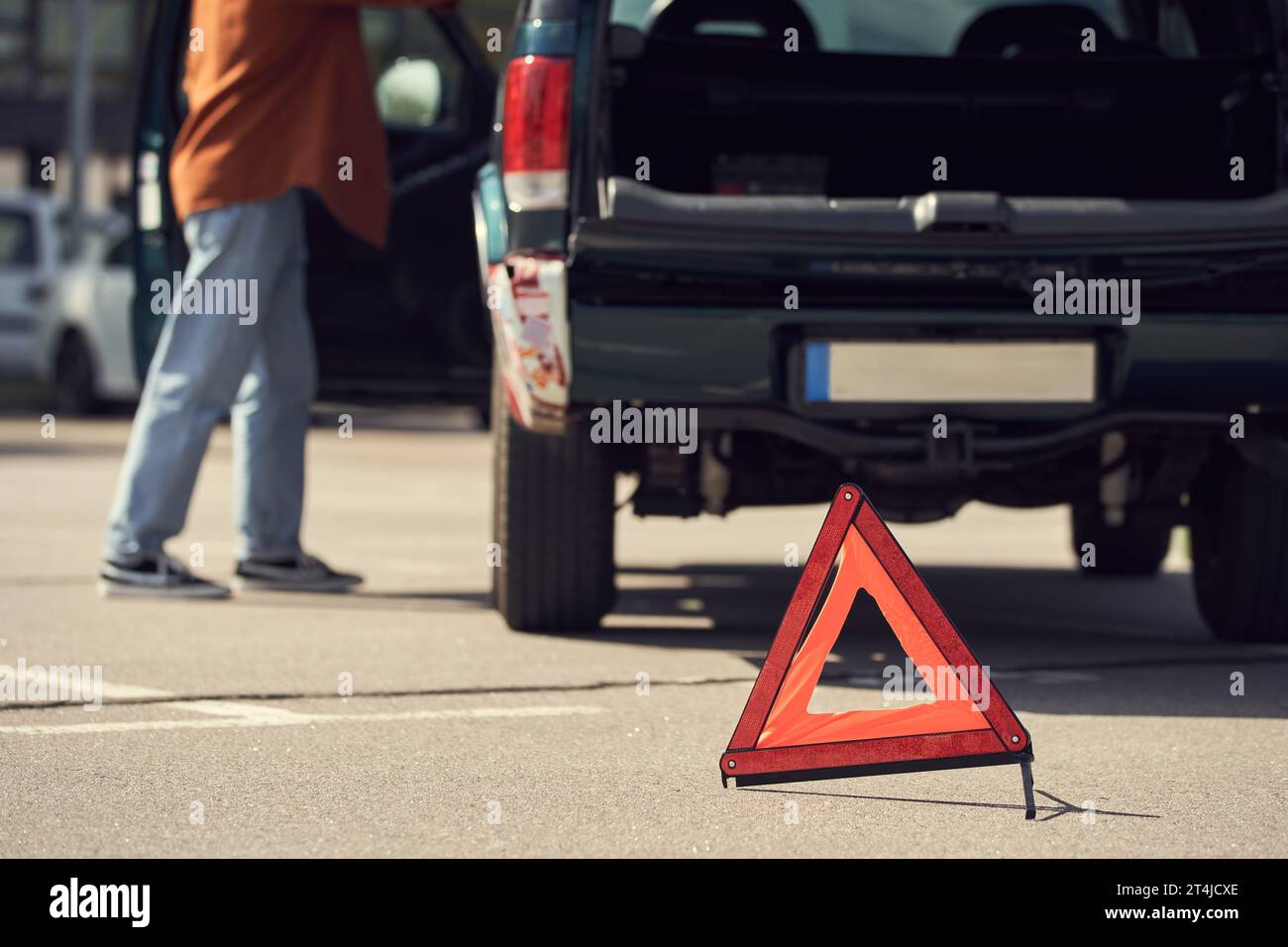 cropped view of young stylish man standing next to his car with warning triangle, blurred photo Stock Photo