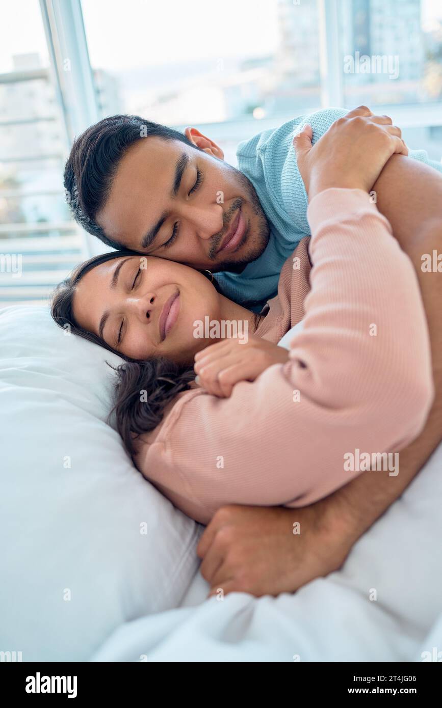 Young mixed race couple lying in bed together and cuddling early in the morning. Handsome asian man holding his beautiful hispanic wife while he Stock Photo